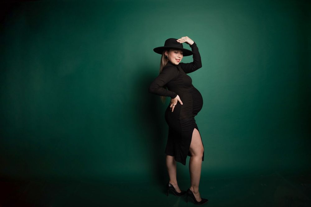 Dramatic maternity portrait in black dress against emerald green background.