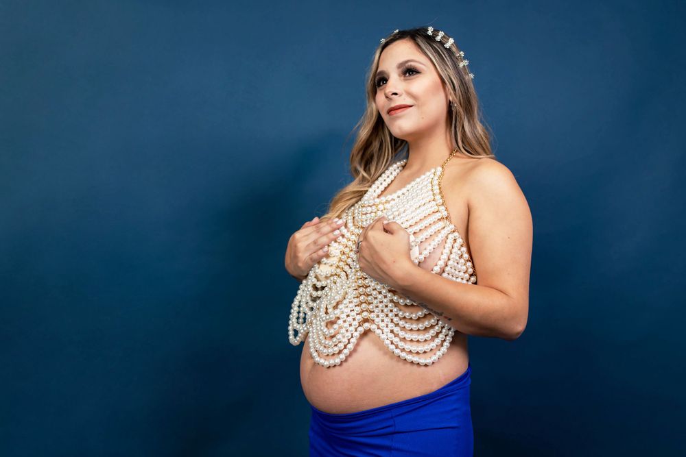 Maternity portrait in white lace top and blue skirt against navy backdrop.