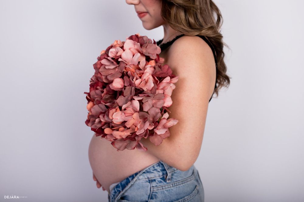 Side view of pregnant belly with pink floral bouquet against white background.