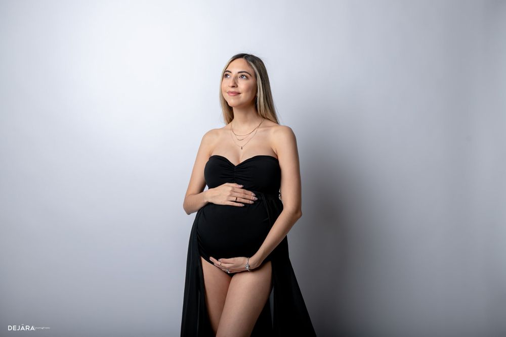 Elegant maternity photo featuring black strapless gown against light backdrop.