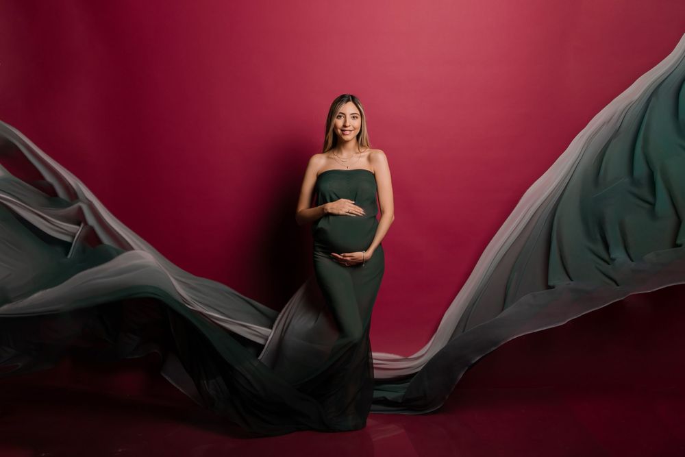 Dramatic maternity portrait with flowing black fabric against deep red backdrop.