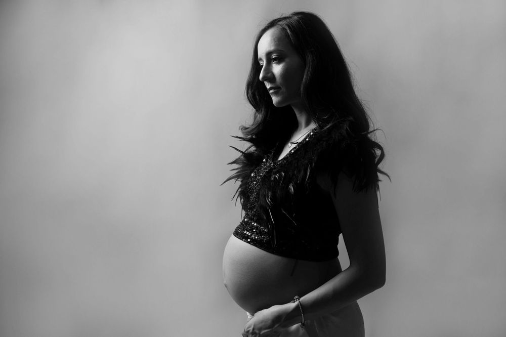 An artistic black and white maternity portrait showing an expectant mother in dramatic lighting.