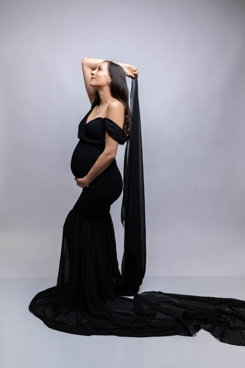 A dramatic maternity photo featuring a black flowing dress with long train against grey background.