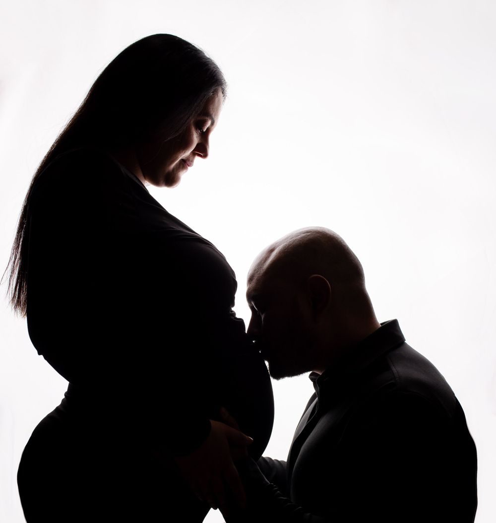 A silhouette captures an intimate moment between expecting parents against white background.