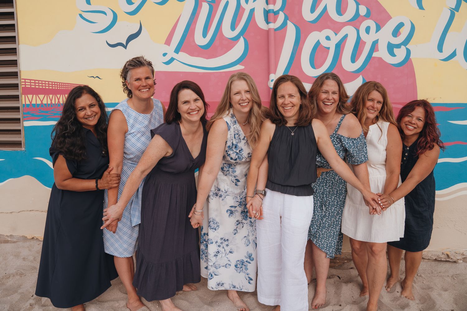 A group of friends posing and smiling together in front of a colorful mural wall with blue and pink lettering.