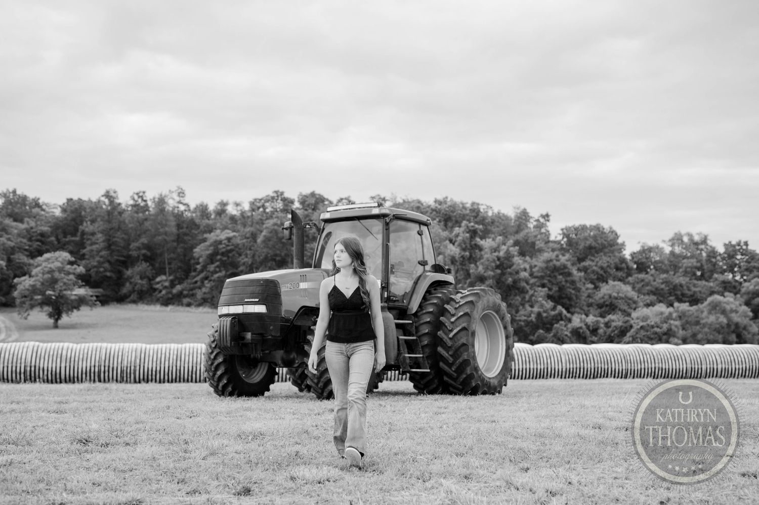 Black and white image of someone walking past a parked tractor in a rural field.