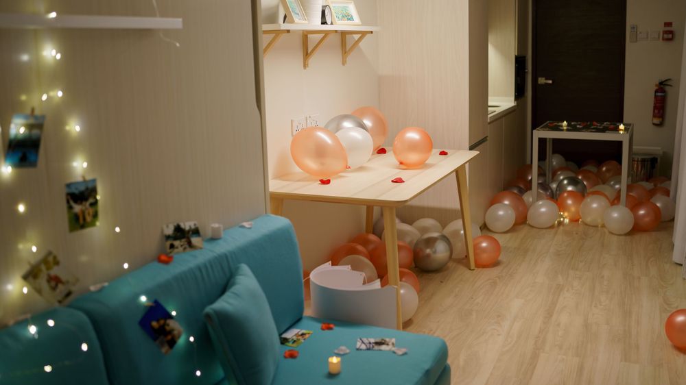 A cozy room decorated with string lights, peach balloons, and a teal couch on light wooden flooring.