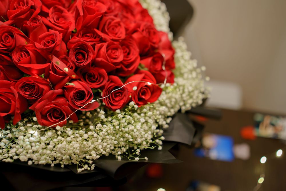 Beautiful bouquet of bright red roses surrounded by delicate baby's breath flowers against a dark background.