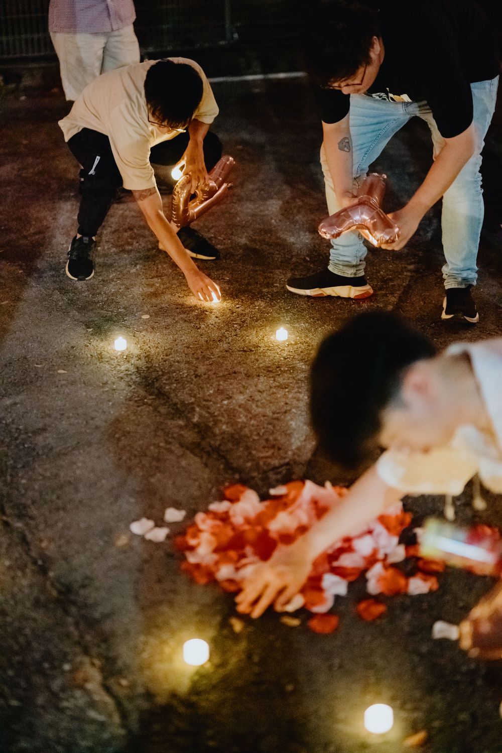 People scatter rose petals on dark floor illuminated by soft glowing lights at a celebration event.