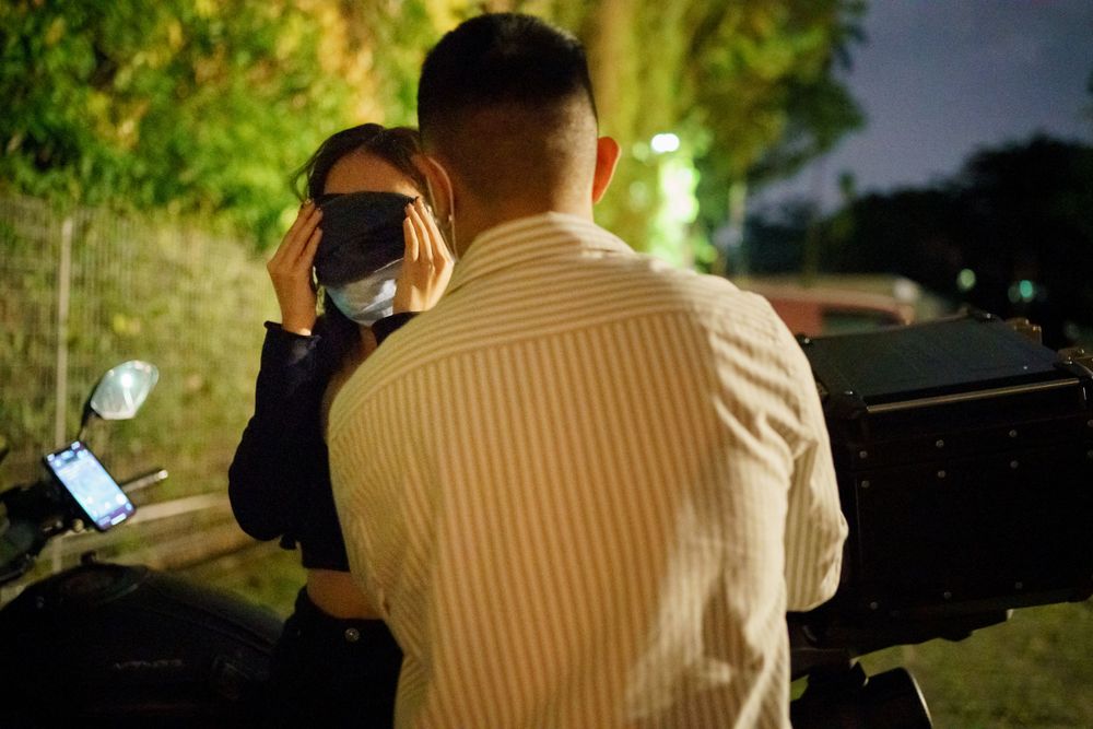 A photographer wearing a striped shirt takes a photo at night with bokeh lights in the background.