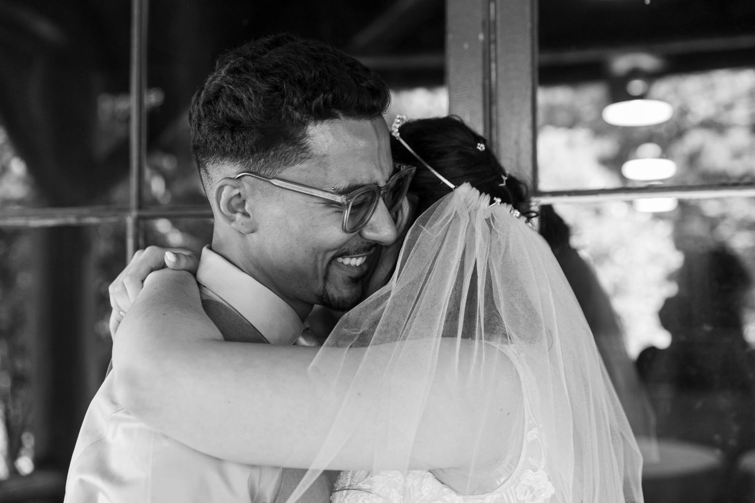 A black and white photo shows a tender moment between newlyweds embracing, with the bride's veil flowing softly.