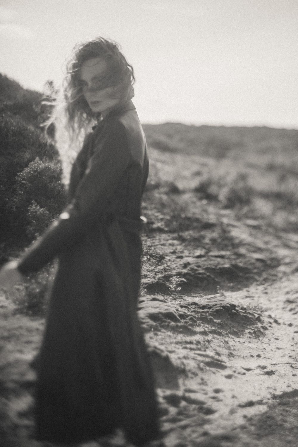 Dreamy sequence of a figure walking through windswept dunes in dark clothing.