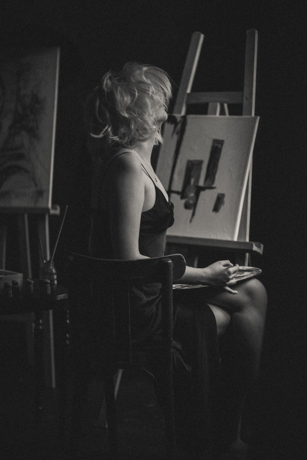 A silhouetted figure in dark lighting sits near art easels in a studio setting.