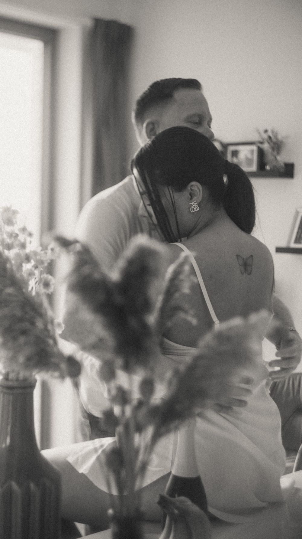Interior scene with blurred figures and flowers by a window in soft focus.