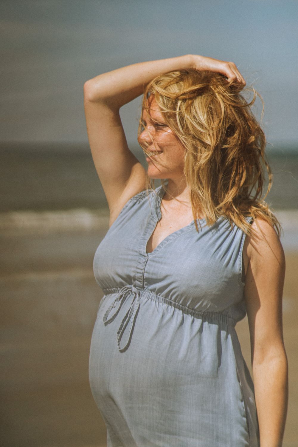 Woman in light blue summer dress poses against natural lighting outdoors.