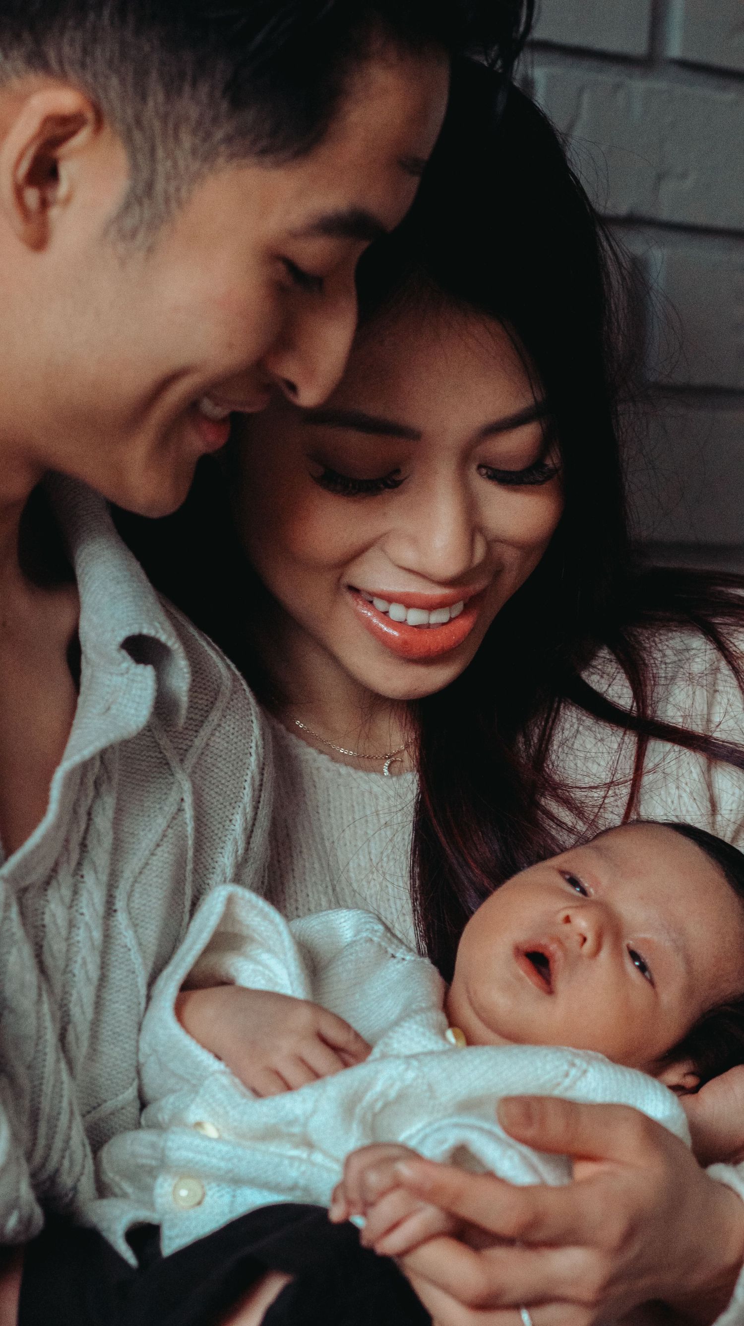 Young couple holding newborn boy for family photo glancing at him