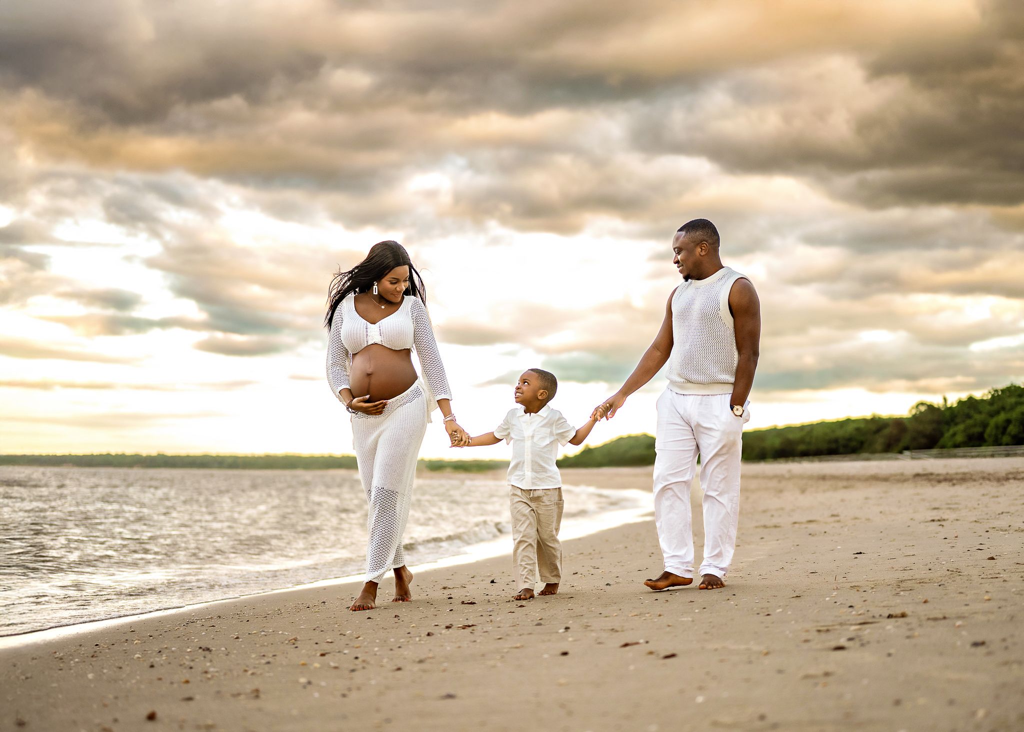 Silhouetted family holding hands while walking on beach at sunset with dramatic cloudy sky over ocean.