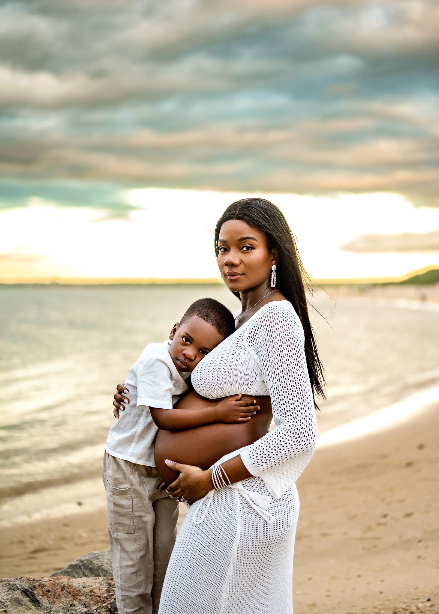 A tender moment captured between a parent and child on a sandy beach at sunset in shades of white and beige.