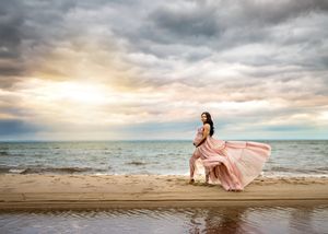 A magical beach wedding photo series with delicate pink dress set against dramatic cloudy skies and ocean waves at sunset.