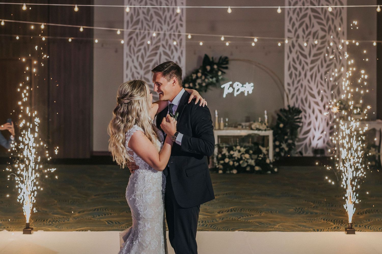 Couple dancing at wedding reception with sparklers and ambient lighting.