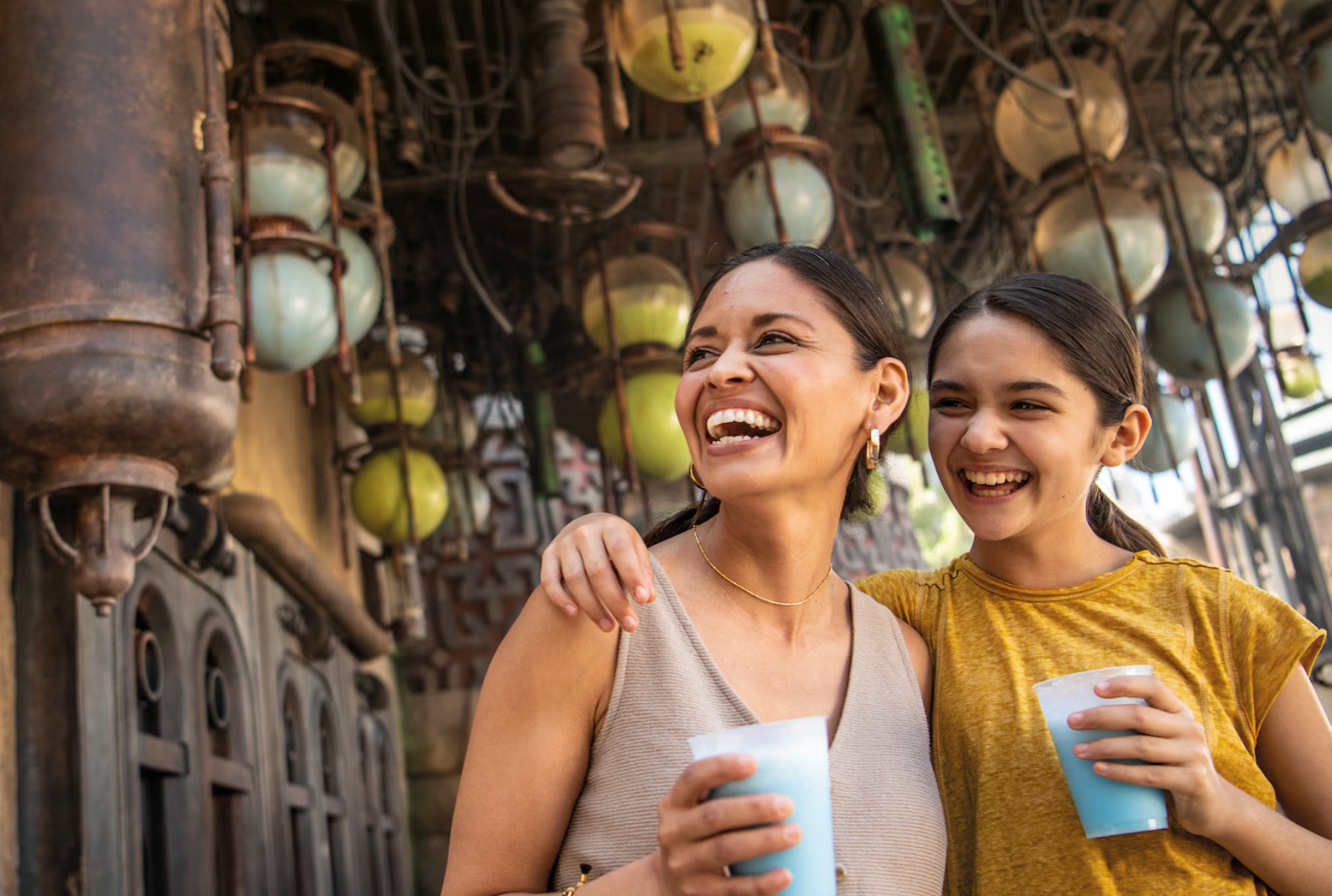 Two friends share drinks and laughter while surrounded by decorative lanterns in an outdoor setting.