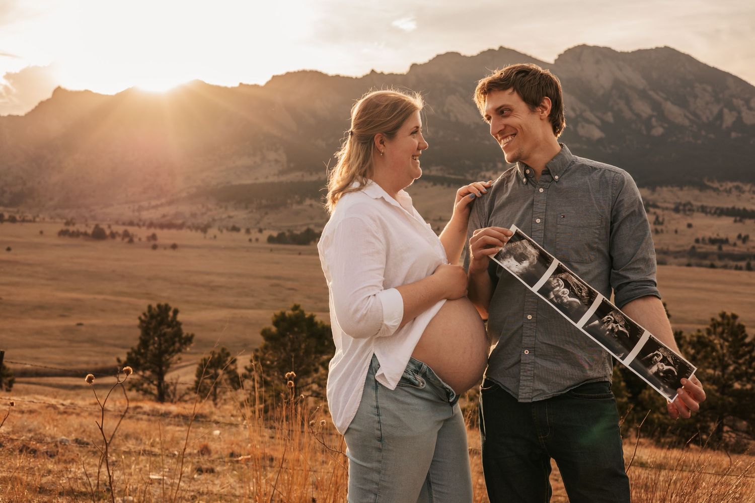Couple holding ultrasound photos at golden hour with mountain backdrop | Maternity Photos in Boulder Colorado