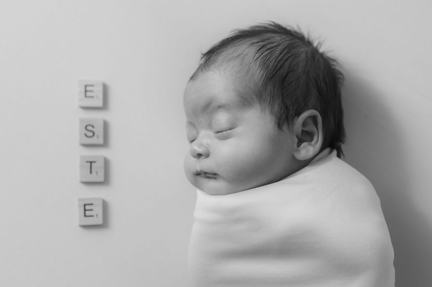 A sleeping newborn baby lies peacefully in black and white with the word ESTE spelled out in letter blocks.