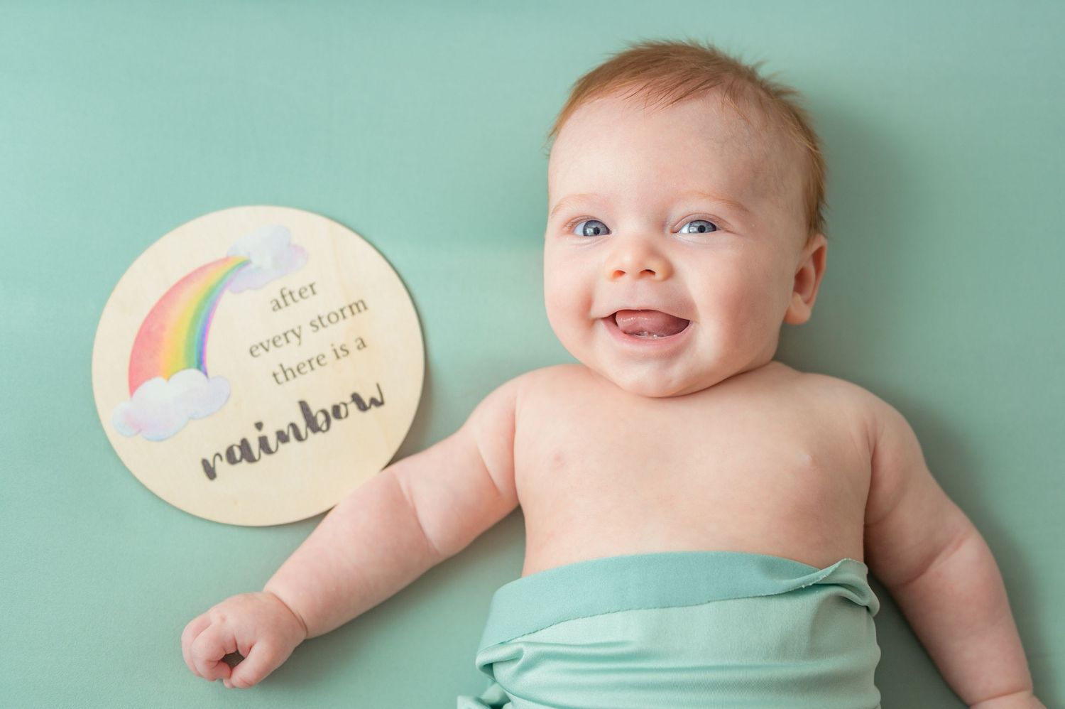 Baby milestone cards document monthly growth with colorful rainbow designs on mint green background.