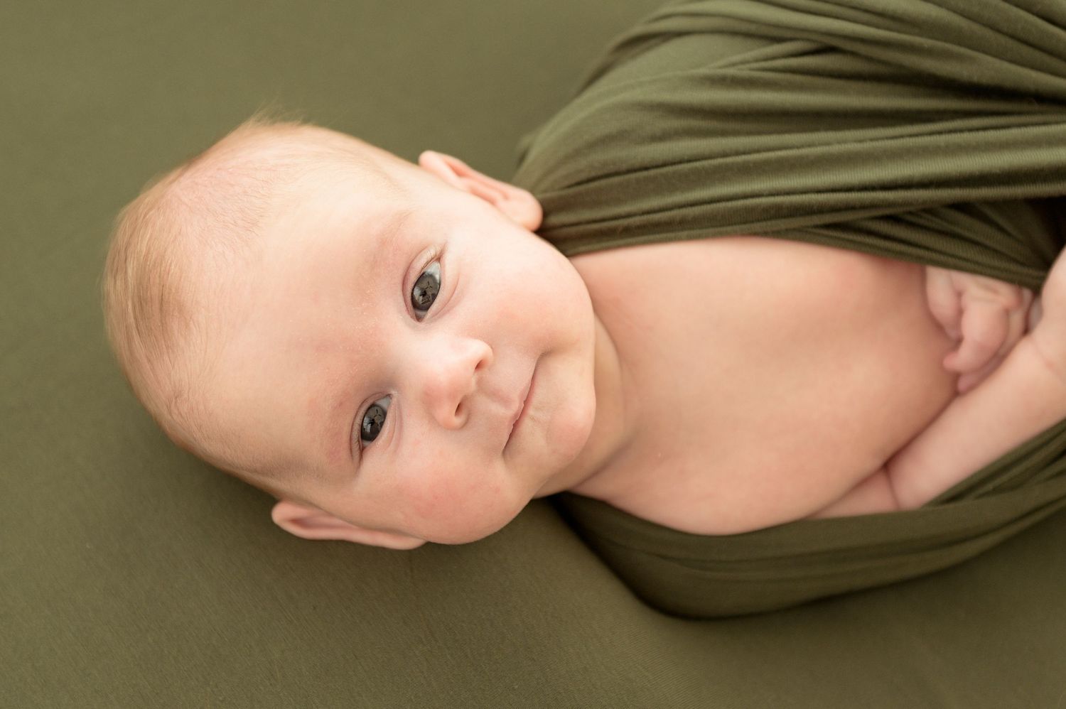 A series of six connected photos showing a baby in an olive green wrap against a neutral background.