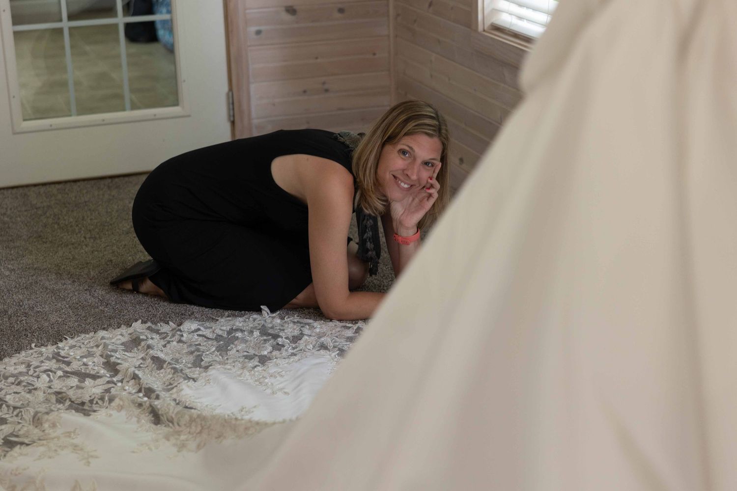 Someone in a black outfit lies on a carpeted floor smiling while looking at something off camera.