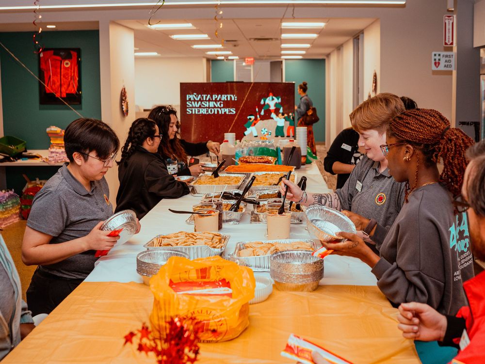 Students gather around tables with pumpkins and carving tools during a festive fall activity in a bright classroom space.