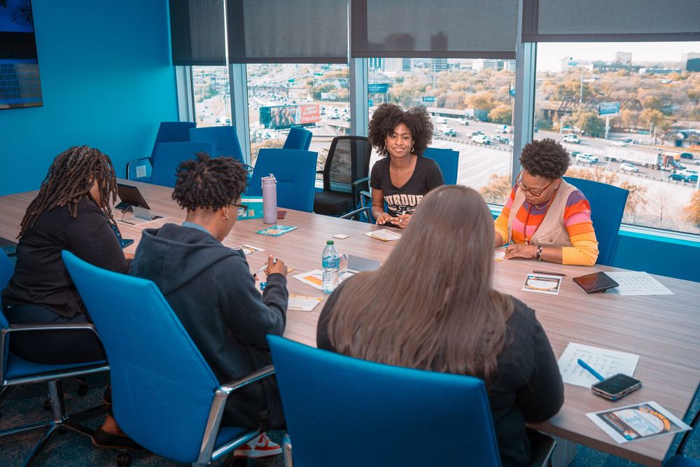 People working at modern office desks with panoramic city views through large windows in bright workspace.