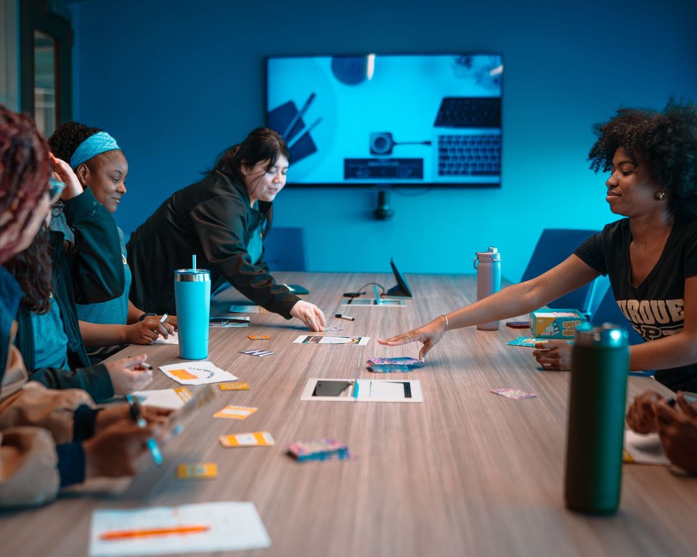 Students work together at a long table in a classroom with blue lighting and water bottles visible.