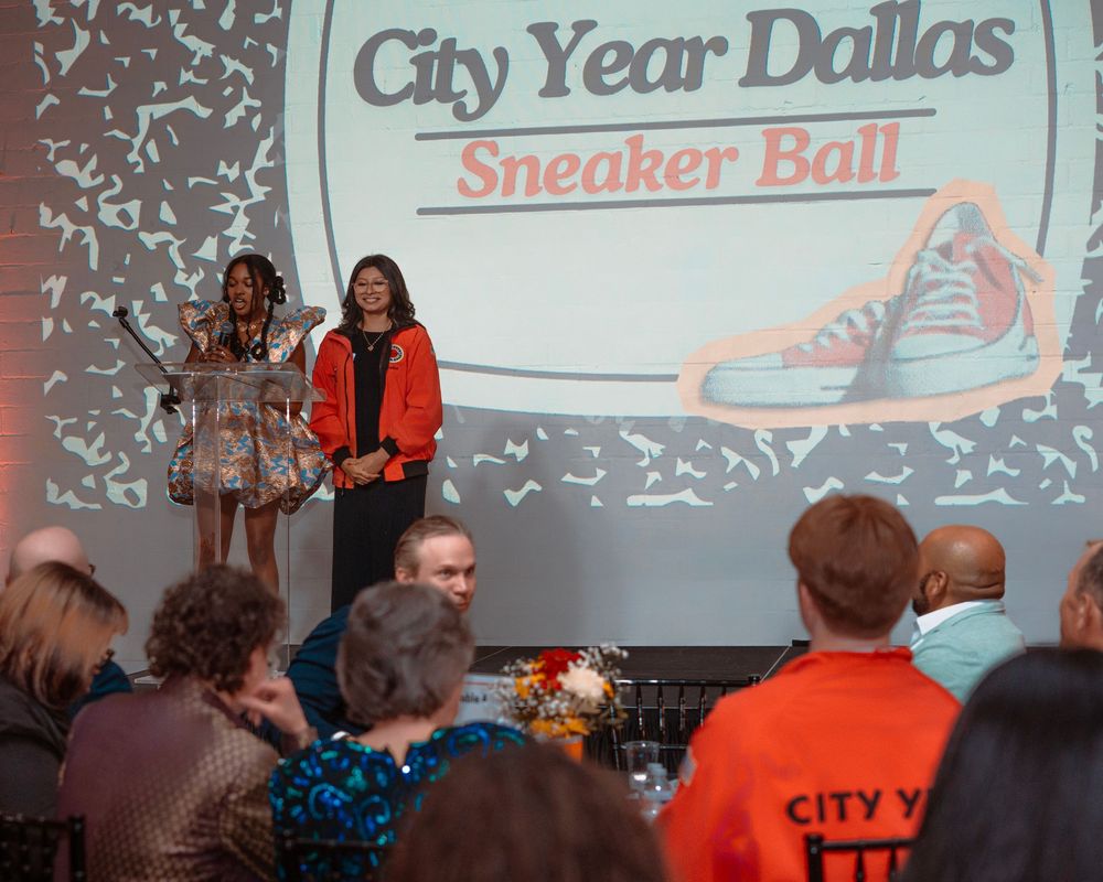 People gathered at City Year Dallas Sneaker Ball event with projected signage and decorations visible in the background.