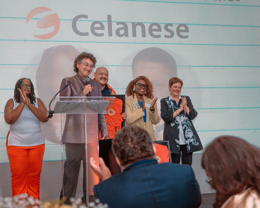 A group of people in orange and dark clothing stand together at a corporate event with Celanese branding.