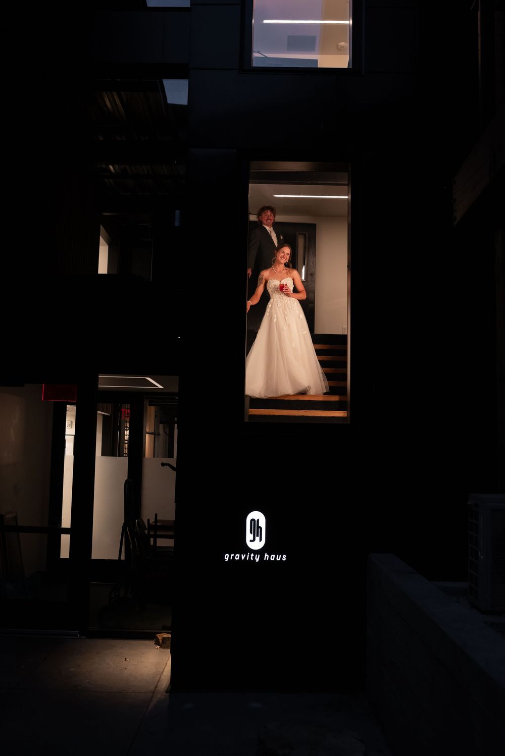A dark hallway leads to an illuminated white bridal gown display in a modern boutique setting.