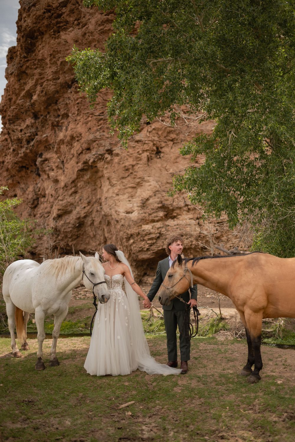 A couple in wedding attire poses with horses against a rustic red rock backdrop in a series of romantic photos.