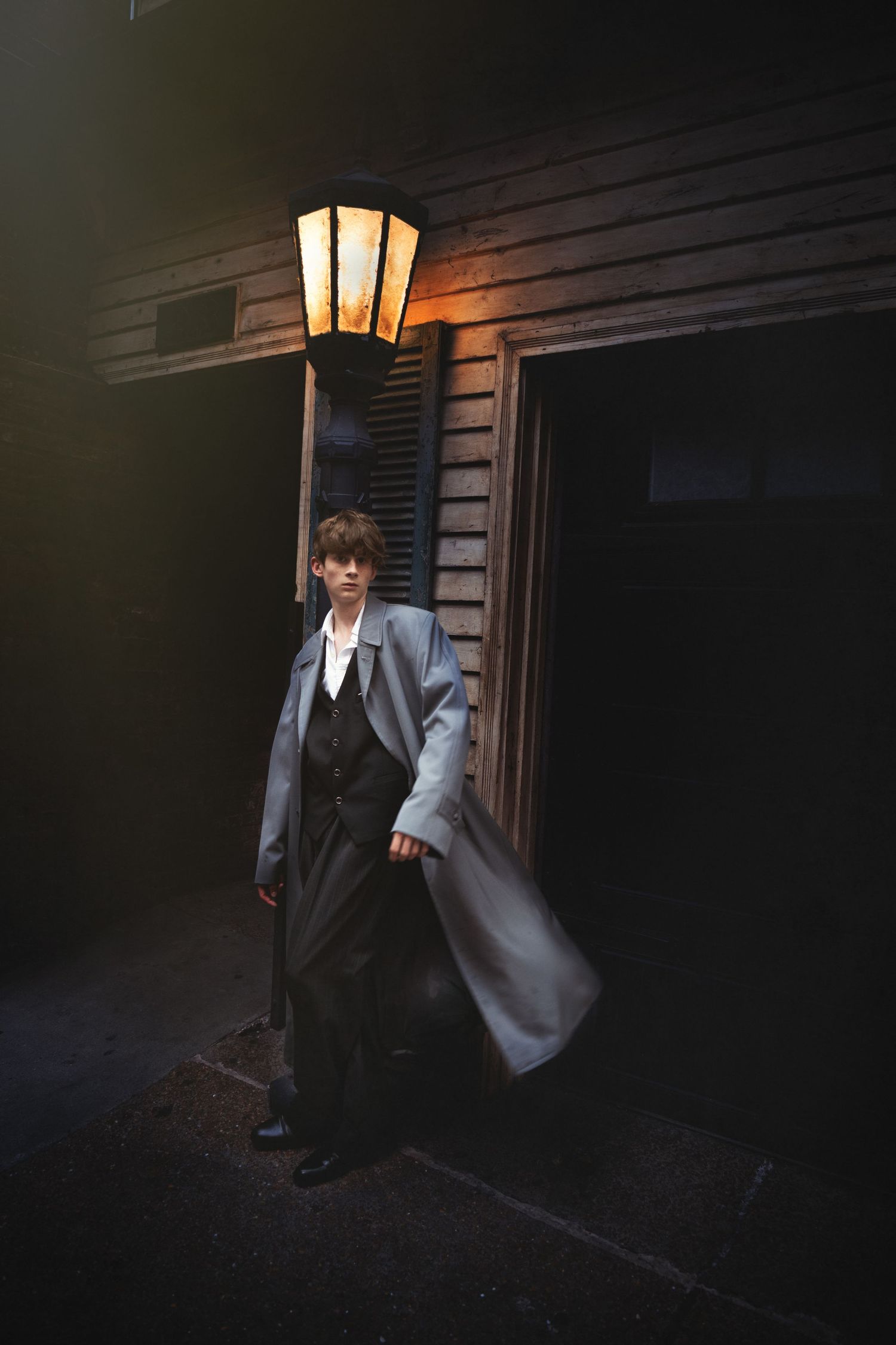 A dark and moody photo series shows a figure in formal attire standing near an illuminated porch light at night.