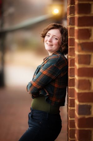 Portrait series against brick wall showing playful poses in plaid shirt and olive vest.