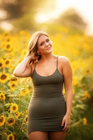 A person poses in a black dress amid a vibrant field of blooming sunflowers during golden hour.