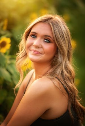 Portrait photo in a sunflower field with warm golden lighting and soft bokeh background.