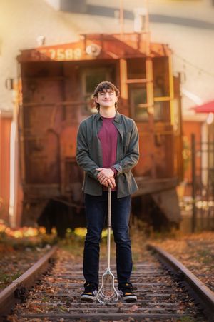 A person stands on train tracks holding a vintage suitcase during autumn with fallen leaves scattered around.
