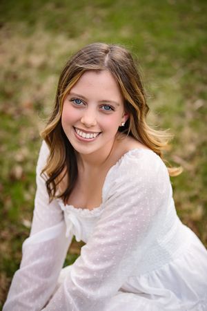 Portrait in white lace dress sitting outdoors with natural lighting and soft background.