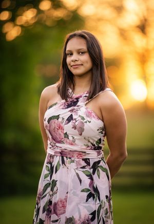 A person in a floral pink and white dress poses outdoors during golden hour sunset with bokeh lighting effects.
