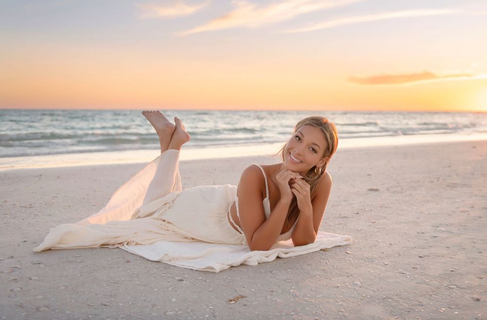 Woman in white dress lying on sandy beach at sunset enjoying peaceful ocean view.
