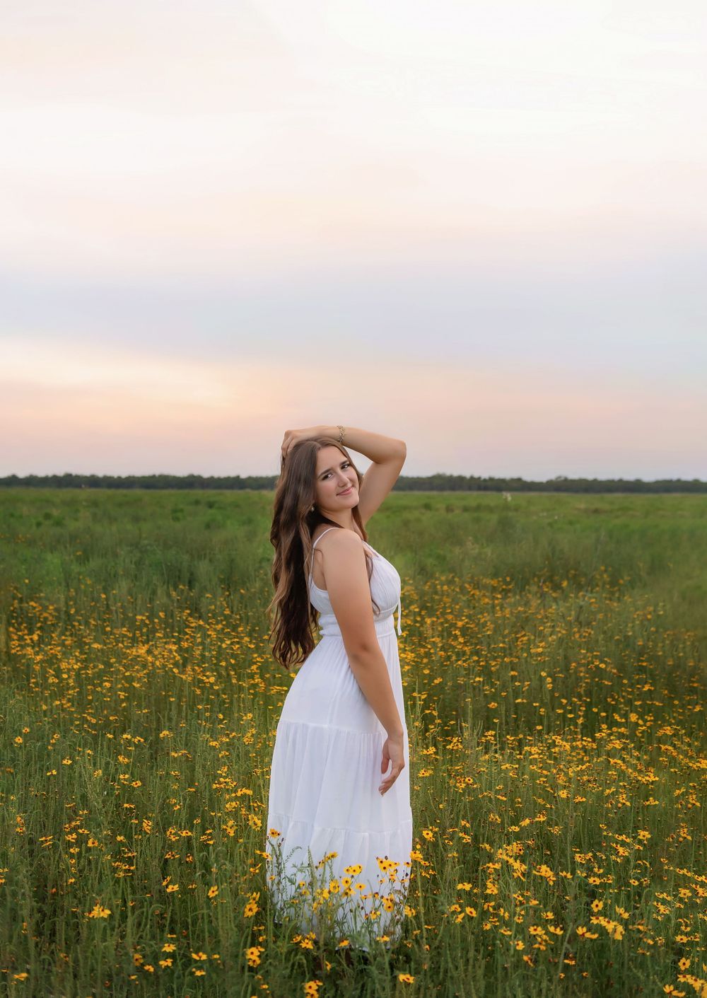 A person in a white dress stands in a vibrant field of yellow wildflowers at sunset.