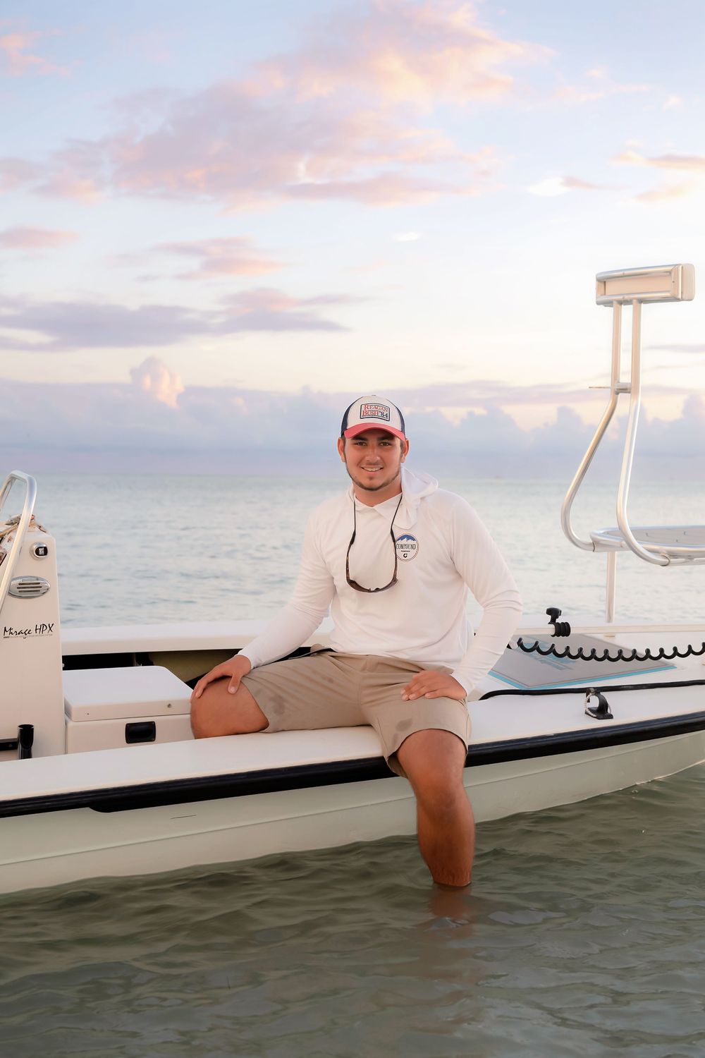 Person relaxing on the edge of a boat dock at sunset with ocean and cloudy sky in the background.