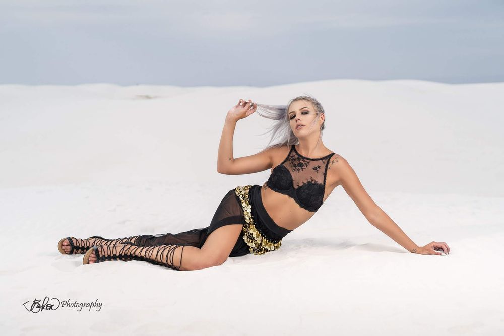 Model in black lace bodysuit poses elegantly on white backdrop in fashion photography series.