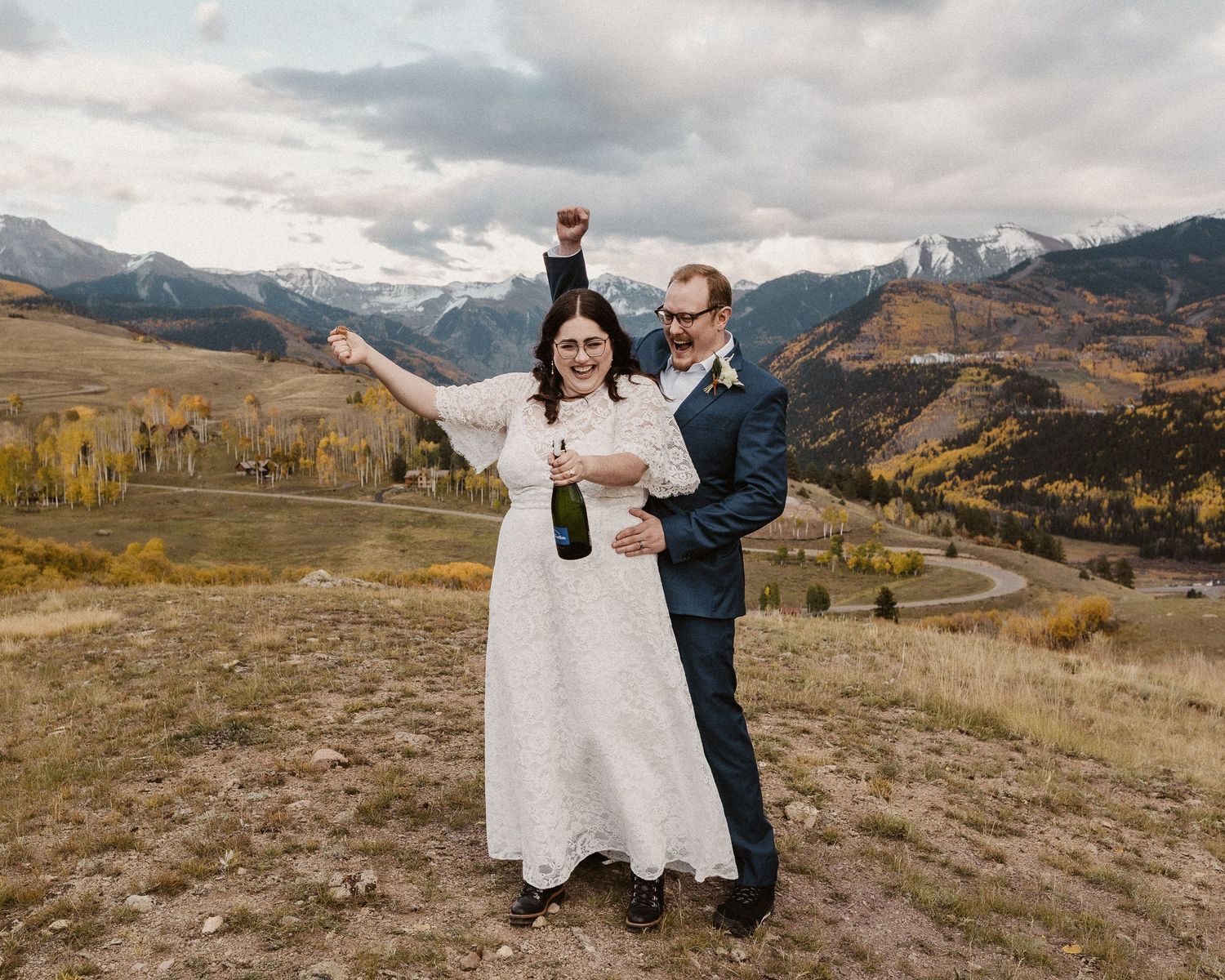 A couple celebrates their wedding day with joyful poses against a scenic mountain backdrop in Colorado.