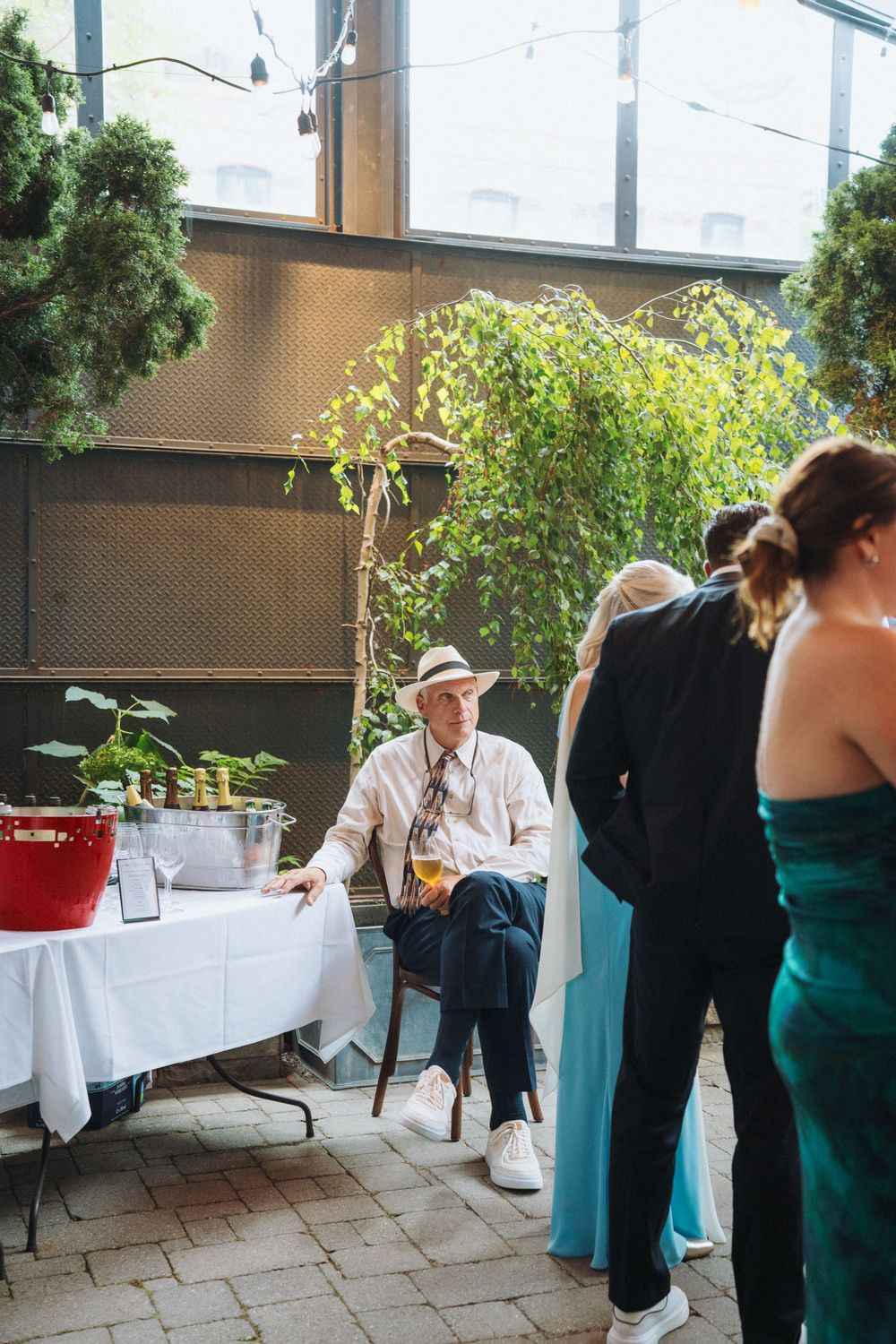Elderly man in white hat sits at table with plants at an outdoor wedding reception.